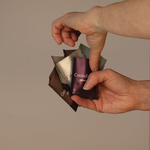 Hands holding a stack of CocoaDreams chocolate packets against a beige background