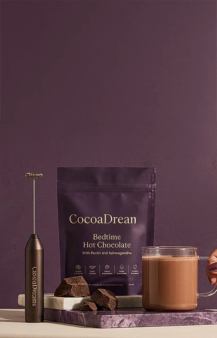 CocoaDreams bedtime hot chocolate pouch with frother, chocolate pieces, and a glass mug on a purple backdrop